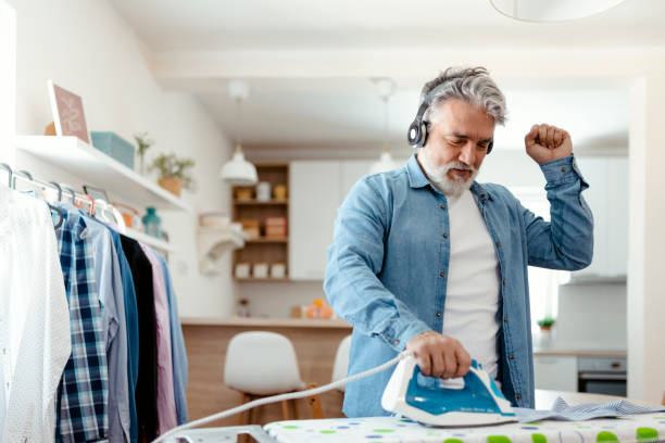 Make Ironing Fun Mature man listening to music ironing clothes at living room modern man doing the ironing stock pictures, royalty-free photos & images