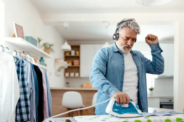 Mature man listening to music ironing clothes at living room