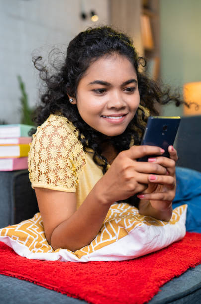 istock vertical close up shot of smiling girl using mobile phone while sleeping on sofa at home - concept of technology addiction, online dating and relaxation 1472091002