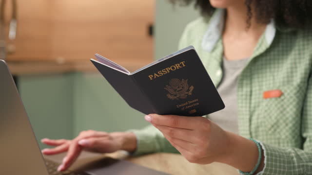 Hands Holding US Passport. Mixed Race woman typing holding US passport document. Close Up.
