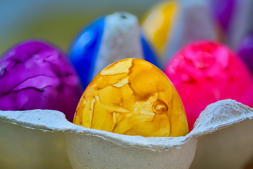 Close up of twelve brightly colored eggs of yellow purple green red orange and yellow in a white ceramic dish