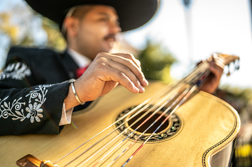 Close up of young man traditional mariachi guitarist playing outdoors