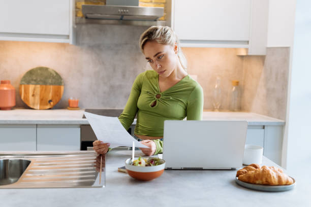 istock Serious British woman behind kitchen counter using laptop and analysing lease agreement 1472100235