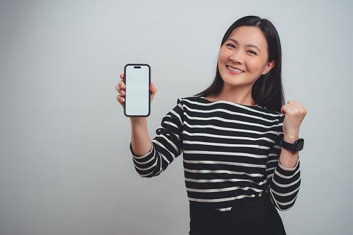 Asian woman happy smiling holding and showing white screen on smartphone standing isolated over white background.
