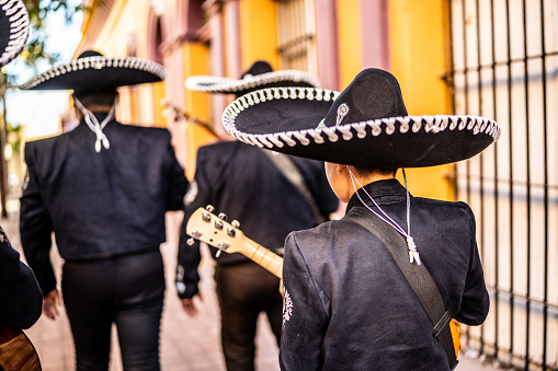 Rear view of group of traditional mariachis walking along the historic district