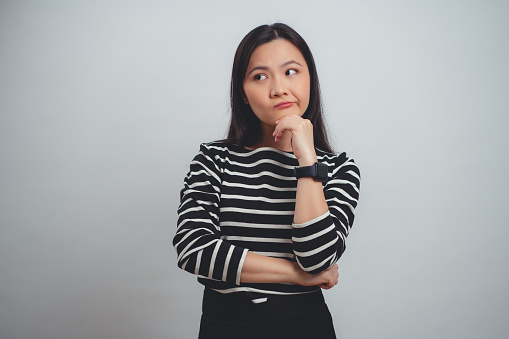 Asian woman thoughtful, worried and confused standing arms crossed isolated over white background.