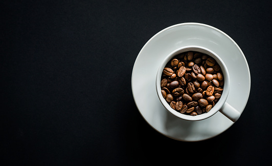 Flat lay of roasted coffee beans in white coffee on black background with copy space
