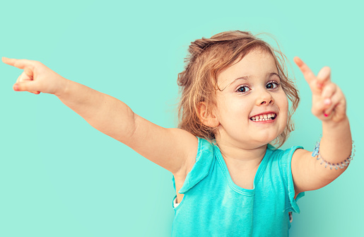 Funny girl on turquoise background. Smiling little girl pointing her finger to the left