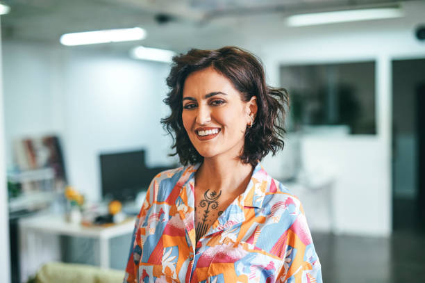 Portrait of cheerful businesswoman in office Cheerful businesswoman with tattoo, wearing colorful shirt, smiling at camera in office middle eastern clothes stock pictures, royalty-free photos & images