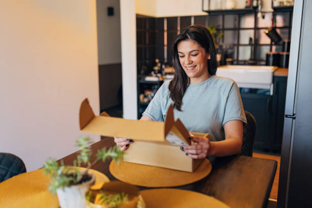 istock Cheerful woman sits at the dining table and opens a cardboard box, a package she ordered online 1472104401