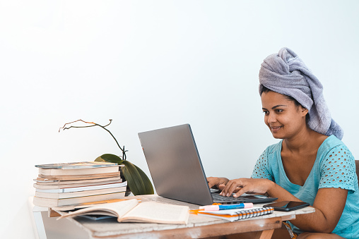 Woman studying online indoors with towel wrapped around her head
