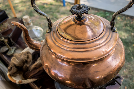 Antique copper teapot close-up outside the house on a background of grass. Vintage teapot closeup, beautiful metal antique utensils.