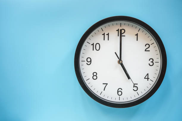 istock Classic black and white analog clock on blue background at Five o'clock with copy space 1472105733