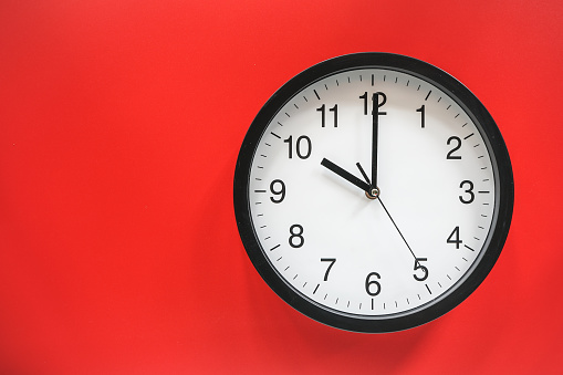 Classic black and white analog clock on red background at Ten o'clock with copy space