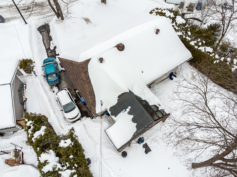 Aerial view of residential home of Quebec city (Charlesbourg) during day of Winter with cars besides and the pilot of the drone looking up in the backyard.