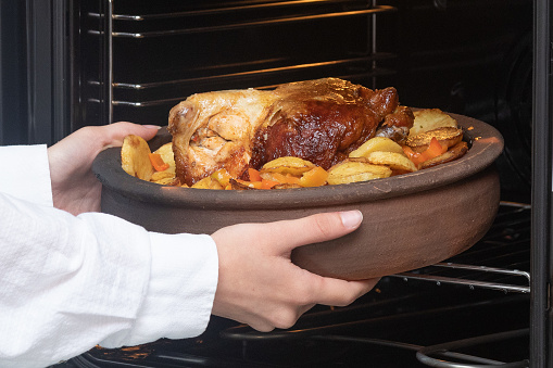 high resolution photo of chicken dish with potatoes and woman's hand in pot baked in oven