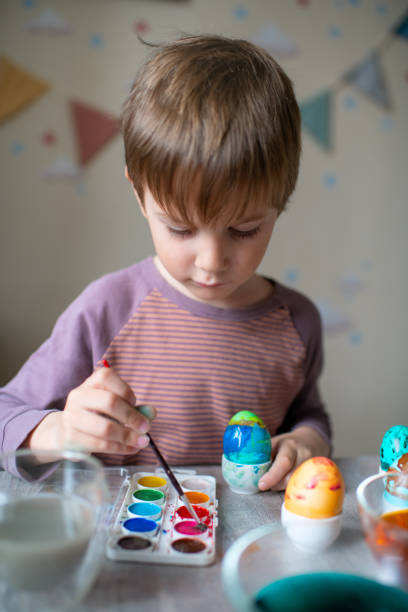 istock Cute child  painting Easter egg at home in springtime 1472107419