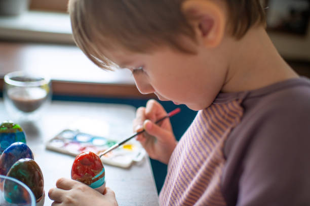 Happy little boy coloring eggs on Easter holidays