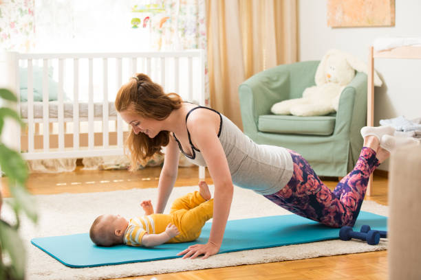Young mother working out at home on a mat with baby stock photo