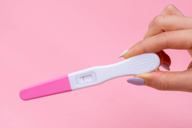 istock Womans hand holding negative pregnancy test with one stripe on pink background with copy space 1472110972