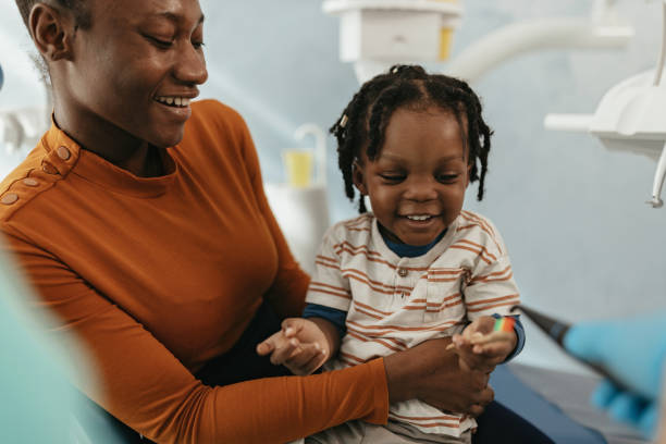 Love to play with toothbrush Mother and son are with dentist at his office, child is playing with toothbrush and sitting in the mother's lap. Visiting dentist for a routine check up baby teeth stock pictures, royalty-free photos & images