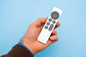 Mans hand holding Siri Apple TV remote controller on the blue background