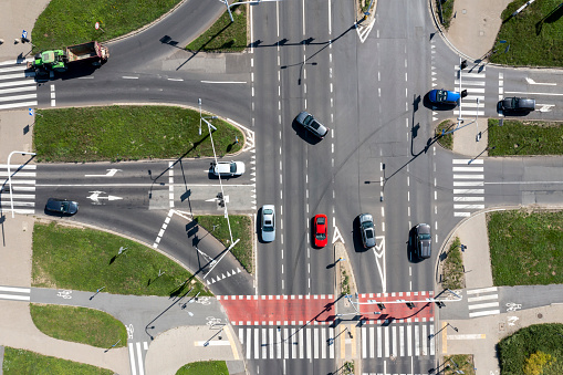 Traffic of cars at the road intersection with bicycle lanes and footpaths, aerial view from directly above.