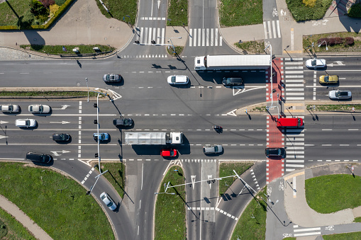 Traffic of cars and trucks at the road intersection with bicycle lanes and footpaths, aerial view from directly above