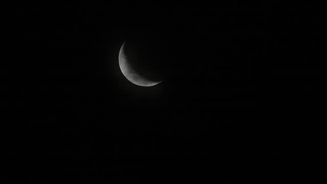 The winds blow the clouds past the crescent moon. A crescent moon in a dark night with many stars in the sky.