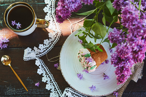 Aesthetic outdoor picnic with a cup of coffee, beautiful cupcake with handmade flowers, flowers and lace decoration. Rural picnic with bright spring, summer tones of flowers on a sunny day