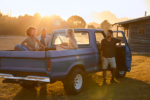 Group Of Friends Arriving In Pick Up Truck On Road Trip To Cabin In Countryside
