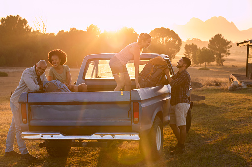 Group Of Friends Unloading Backpack From Pick Up Truck On Road Trip To Cabin In Countryside