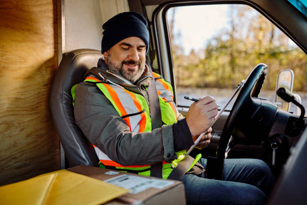 istock Happy delivery man taking notes while sitting in truck cabin. 1472119054