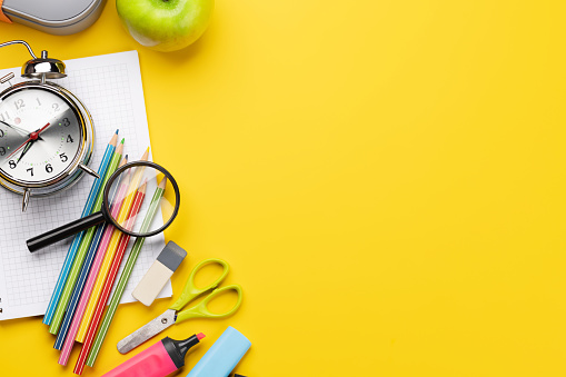 School supplies, stationery, and lunch box on yellow background. Education and nutrition. Flat lay with blank space