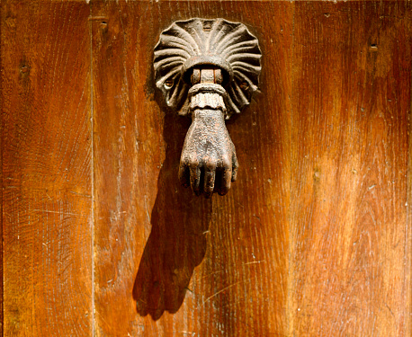 Old door knocker representing a hand on a old wood door in the sunlight in the old Lyon in France.