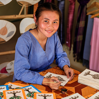 Laotian young girl painting handmade postcards in a workshop near Luang Prabang, Laos