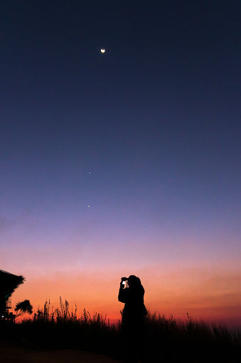 Women taking picture of nature observing evening sky with stars, planets and crescent moon. Moon meets Jupiter and Venus in the twilight sky.