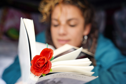 Young woman lying reading a book in her camper van with a rose. Sant Jordi Day in Catalonia