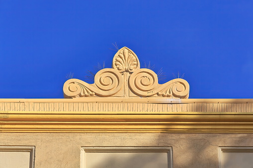 Neo-Baroque style finial atop the flat roof parapet of a 1920s Art-Deco building orange-yellow facade with linear ornation on The Corso pedestrian mall south side. Manly suburb-Sydney-NSW-Australia.