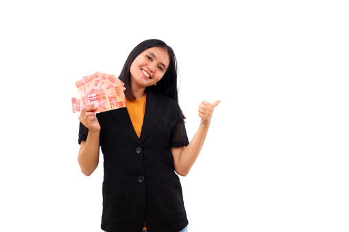 Happy young asian business woman holding Indonesian banknotes while showing thumbs up. Isolated