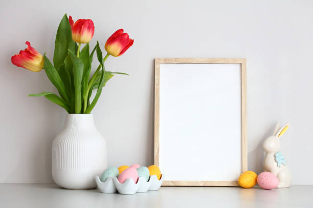 istock Happy Easter home decor on table on white wall background. Picture frame template, vase of red tulips, Easter eggs and bunny. 1472128838