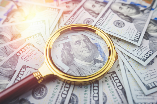 Closeup one hundred US dollar bills under gold magnifying glass, finance conept