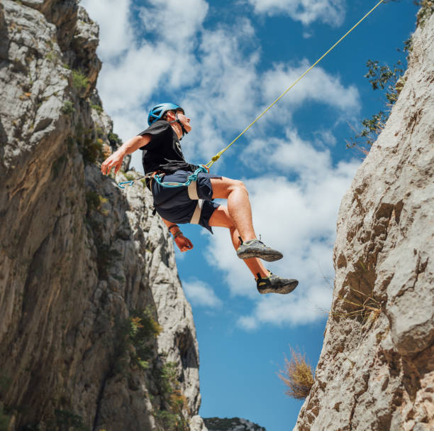 istock Climber teenage boy in protective helmet jumping on vertical cliff rock wall using rope Belay device, climbing harness in Paklenica canyon in Croatia. Active extreme sports time spending concept 1472132485