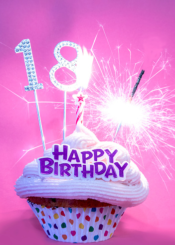 Pink background and pink frosting on cupcake, happy birthday cupcake for 18 year old girl, shiny silver number 18, one candle and sparkler