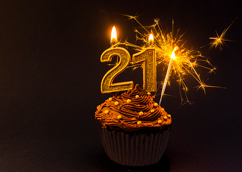 Chocolate cupcake with Number 21 gold candles  and gold sparkler, black background,