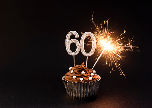 Chocolate cupcake with Number 60 silver sign, and gold sparkler, black background,