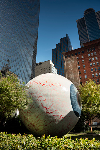 Dallas, Texas, USA - November 13, 2021:  30 foot tall, realistically rendered art installation fiberglass sculpture of a human eyeball in a fenced garden in downtown Dallas Texas USA.  The piece is called simply Eye, and was created by artist Tony Tasset in 2007
