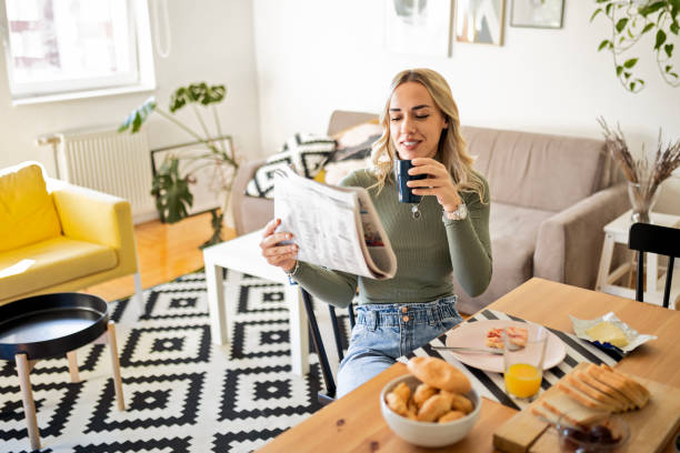 istock Young woman having coffee after breakfast at home reading newspaper 1472145415