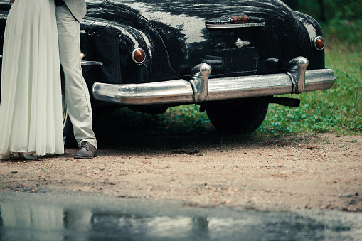 bride and groom embracing near a retro car outdoors on the forest road