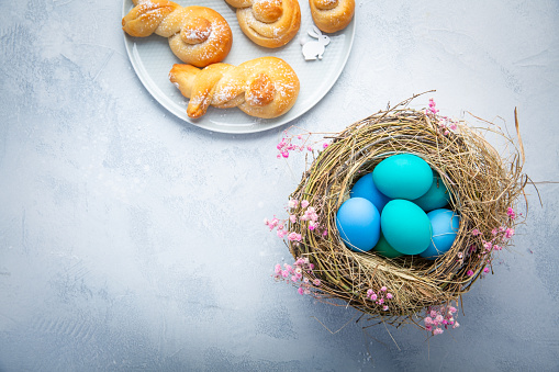 Easter eggs in nest with sweet buns made from yeast dough in a shape of Easter bunny